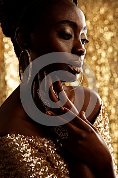 African Beauty Woman with Gold Jewelry over shining Background. Dark Skinned Model with Golden Lips Make up Profile. Afro Fashion