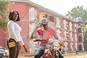 an african bike man standing with a lady making a call