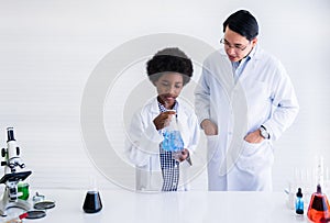 African black boy student and asian male professor in white gown is learning and test science chemical with colorful liquid in