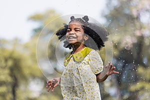 African black child with curly hair is jumping happily in the water spray at outdoor