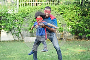 African black family spent time together in the home garden. Laughing father and son playing superhero at the day time. Happy