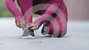 African black female hands tying shoelace on running shoes before practice. Woman athlete preparing for jogging outdoors