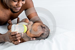 African black skin  father feeding milk from bottle milk to his  baby newborn daughter