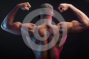 African bodybuilder in Back double biceps position, over dark background.