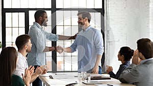 African boss shaking hand of happy employee on staff meeting