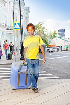 African boy holding pink luggage and walking