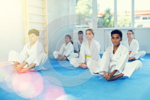 African boy stretching in butterfly pose during group martial arts training