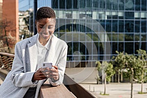 African business woman standing and leaning on the railing of a bridge while using her smart phone