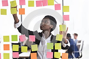 African businesslady jotting on adhesive stickers attached on glass wall