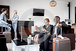 African businessman discussing ideas with female colleague while sitting on sofa in airport business lounge, busy businesspeople