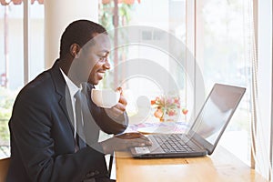 African Businessman  holding coffee with smile and playing labtop