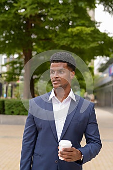 African businessman holding take away coffee cup outdoors in city while thinking