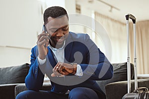 African businessman in hotel, on smartphone call and checking wrist watch for time. Corporate professional in Chicago