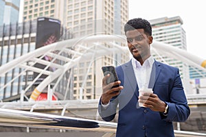 African businessman outdoors using mobile phone and holding take away coffee cup