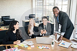 African businessman planning and discussing with Caucasian colleagues with laughing and clapping hands.