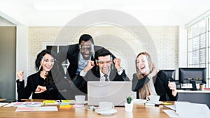 African businessman stands in the back of Caucasian colleagues wearing face shield. looking on laptop at business group meeting