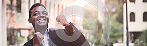 African businessman in a suit happy smile with raised hands up clenched fists on a building background. The Celebrate success and