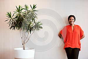 African businesswoman standing next to pot plant smiling at camera