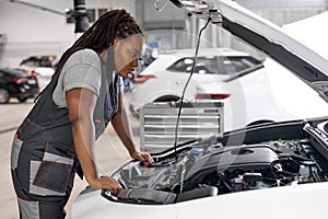 African Car mechanic woman is examining under hood of car at repair garage