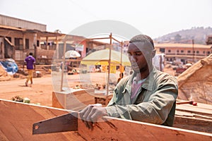 African carpenter in his open-air workshop sawing a board. Tiring handcraft photo
