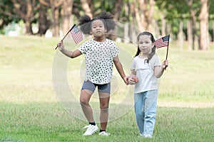 African and Caucasian kids playing together and holding small America flag at green park.