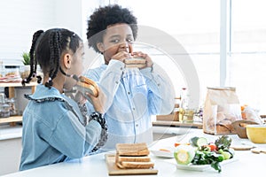 African children holding homemade sandwiches in hands and eating together in kitchen at home. Cute Brother and sister prepare food