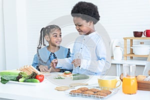 African children making sandwich, preparing food in kitchen together at home. Smiling brother and sister pick ham sliced, tomato,