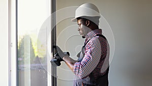 African construction worker installing pvc window or door in house. Handyman fixing the window with screwdriver