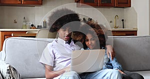 African couple cuddle on sofa hold laptop discuss online purchases