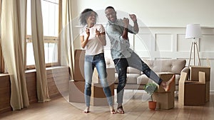 African couple first time home buyers dancing in living room