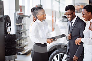 African couple getting car key from dealer in showroom and signing contract