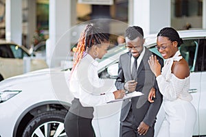 African couple getting car key from dealer in showroom and signing contract