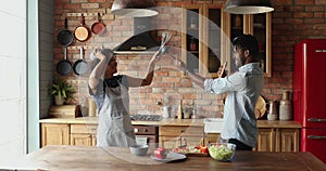 African couple having fun fooling in kitchen holding kitchenware fighting
