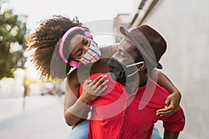 African couple piggyback wearing face mask - Happy Afro people having fun outdoor