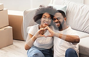 African Couple Sitting Among Moving Boxes Gesturing Heart Shape Indoors