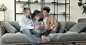 African couple with tween daughter relax on couch use smartphone
