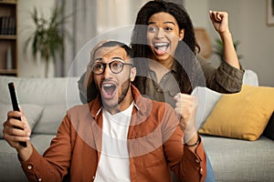 African Couple Watching Sport On TV Shaking Fists Indoor