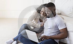 African couple web surfing on laptop while sitting at home