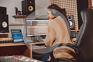 African cute woman blogger records online podcast using laptop, headphones and microphone in professional music studio