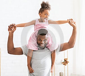 African dad carrying his cute little daughter on shoulders