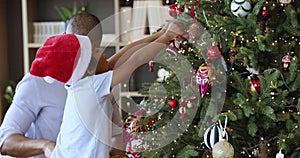 African dad his cute son hanging baubles on Christmas tree