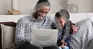 African dad and little kid using laptop seated on sofa