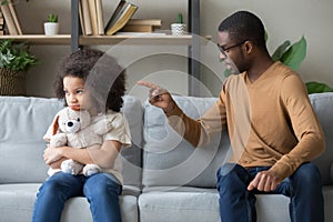 African dad scolding for discipline stubborn daughter sitting on sofa