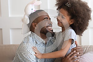 African daughter holding rabbit soft toy playing with father indoors