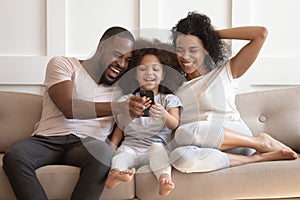 African daughter and parents looking at smartphone laughing on sofa