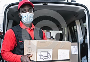 African delivery man carrying cardboard box while wearing face mask to avoid corona virus spread