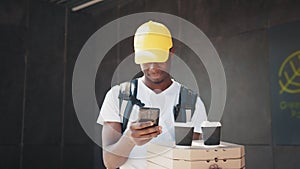 African delivery man with package and smartphone, while carrying a box with pizza and coffee. Nice black Male courier