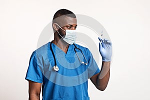 African doc in face mask and gloves looking at syringe