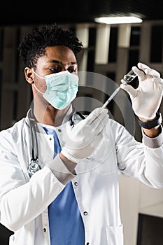 African doctor in a medical mask prepares to inject coronavirus covid-19 vaccine. Black doctor in white medical robe