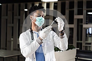 African doctor in a medical mask prepares to inject coronavirus covid-19 vaccine. Black doctor in white medical robe